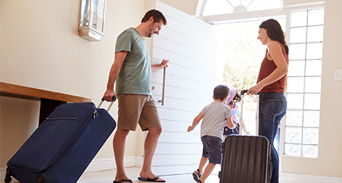parents pulling suitcases out of a home with two children running out of the house